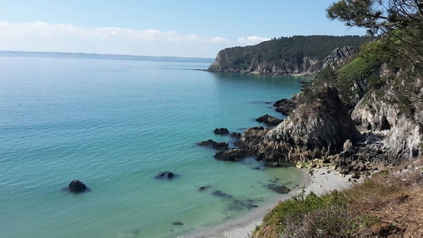 Un paisaje costero con aguas cristalinas, acantilados rocosos y una playa de arena.