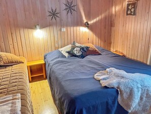 A wooden-paneled room with a bed, a nightstand, and a wall-mounted lamp.