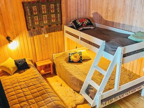 Quarto com uma cama de solteiro, uma cama individual, uma pequena mesa de cabeceira de madeira e uma luminária fixada na parede.