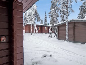 Paisagem coberta de neve com uma cabana de madeira e um edifício vermelho com janelas.