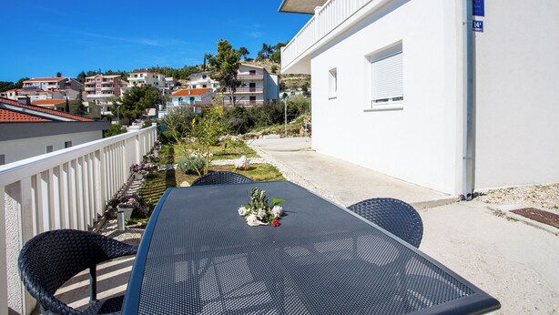 A balcony with a table and chairs, overlooking a residential area with houses and trees. - Apartments Magdales (Dugi Rat)