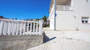 A white building with a balcony, a concrete wall, and a clear blue sky. - Apartments Magdales (Dugi Rat)