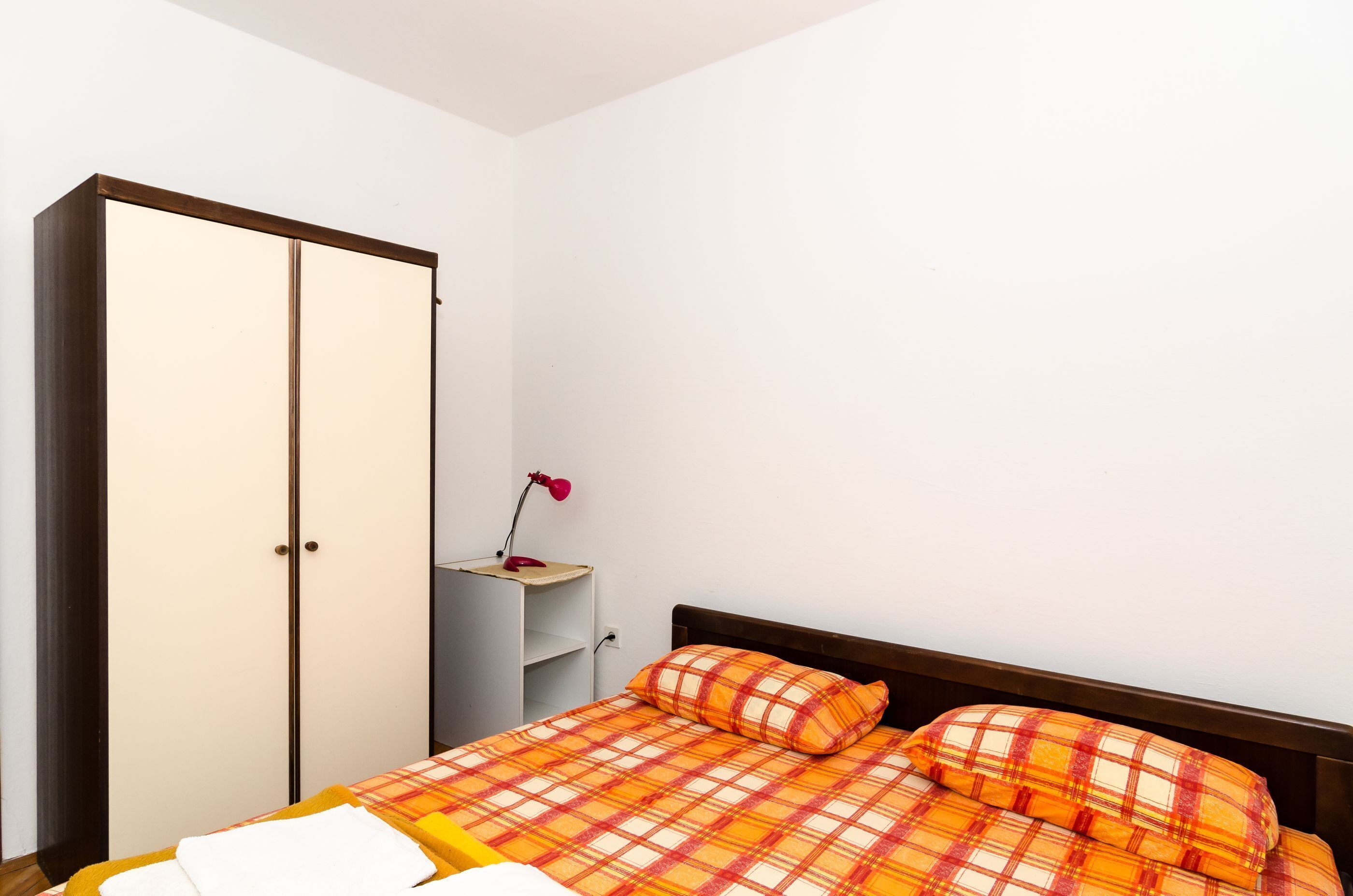 A bedroom with a bed, a wardrobe, and a nightstand with a lamp.