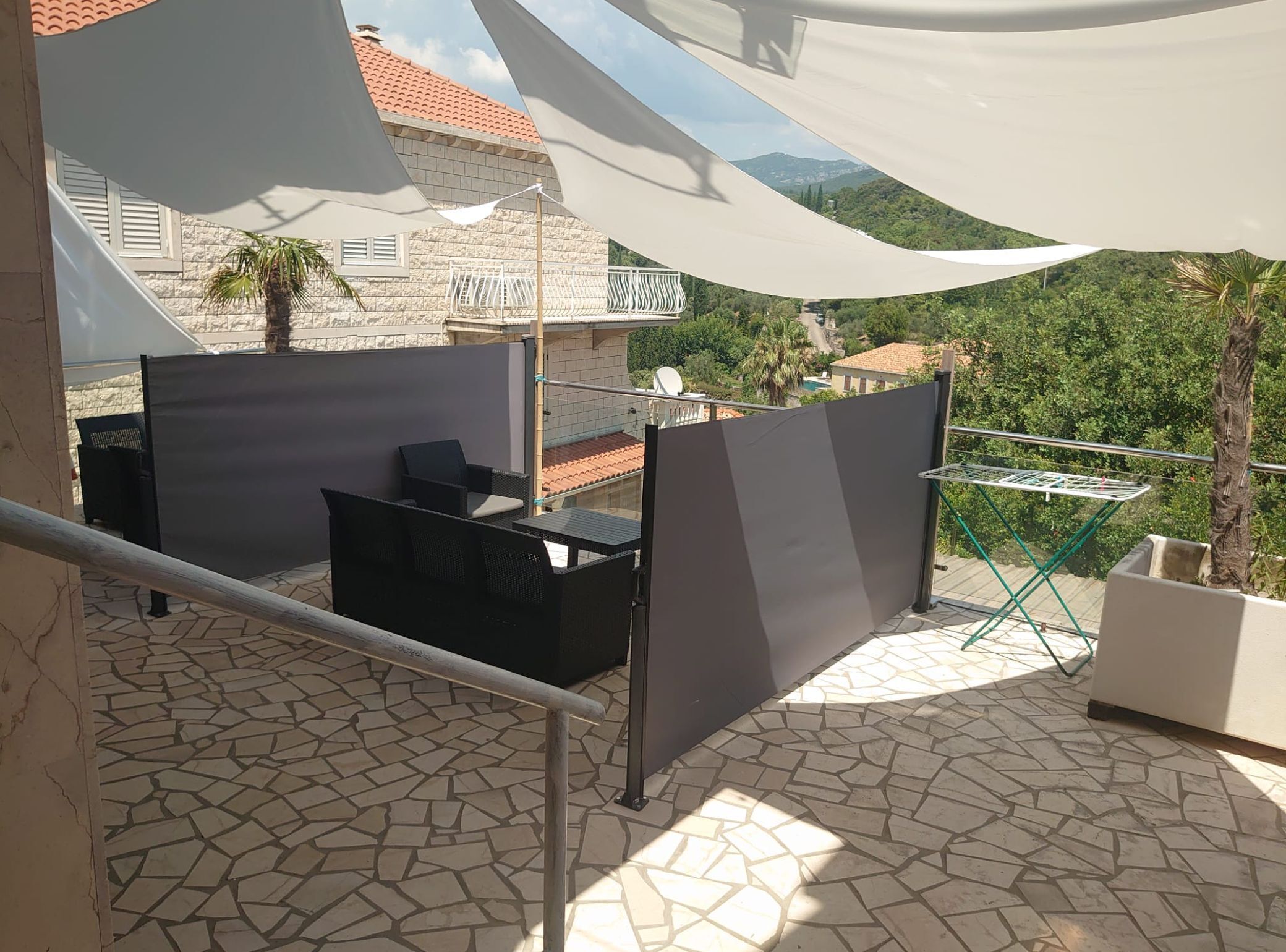 A balcony with a tiled floor, outdoor furniture, a white cloth shade, and a view of a hillside.