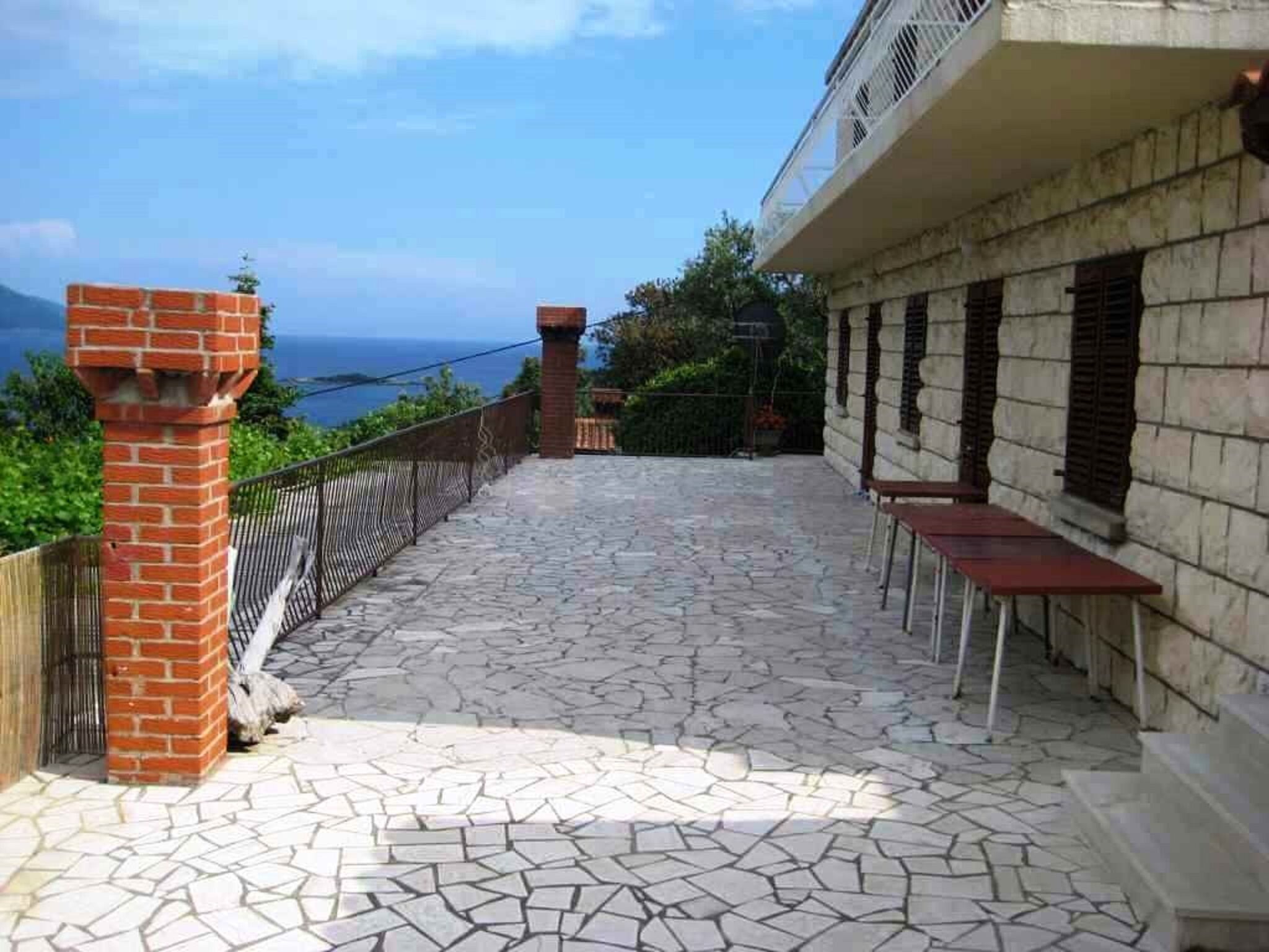 Eine terrasse mit Steinplatten, einem Backsteinsschornstein, Sitzgelegenheiten im Freien und Blick aufs Meer.