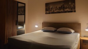 Habitación de hotel con cama, dos lámparas de noche, un cuadro de paisaje urbano en la pared y un armario de madera.