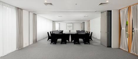 A conference room with a long table, white curtains, and a neutral carpet.