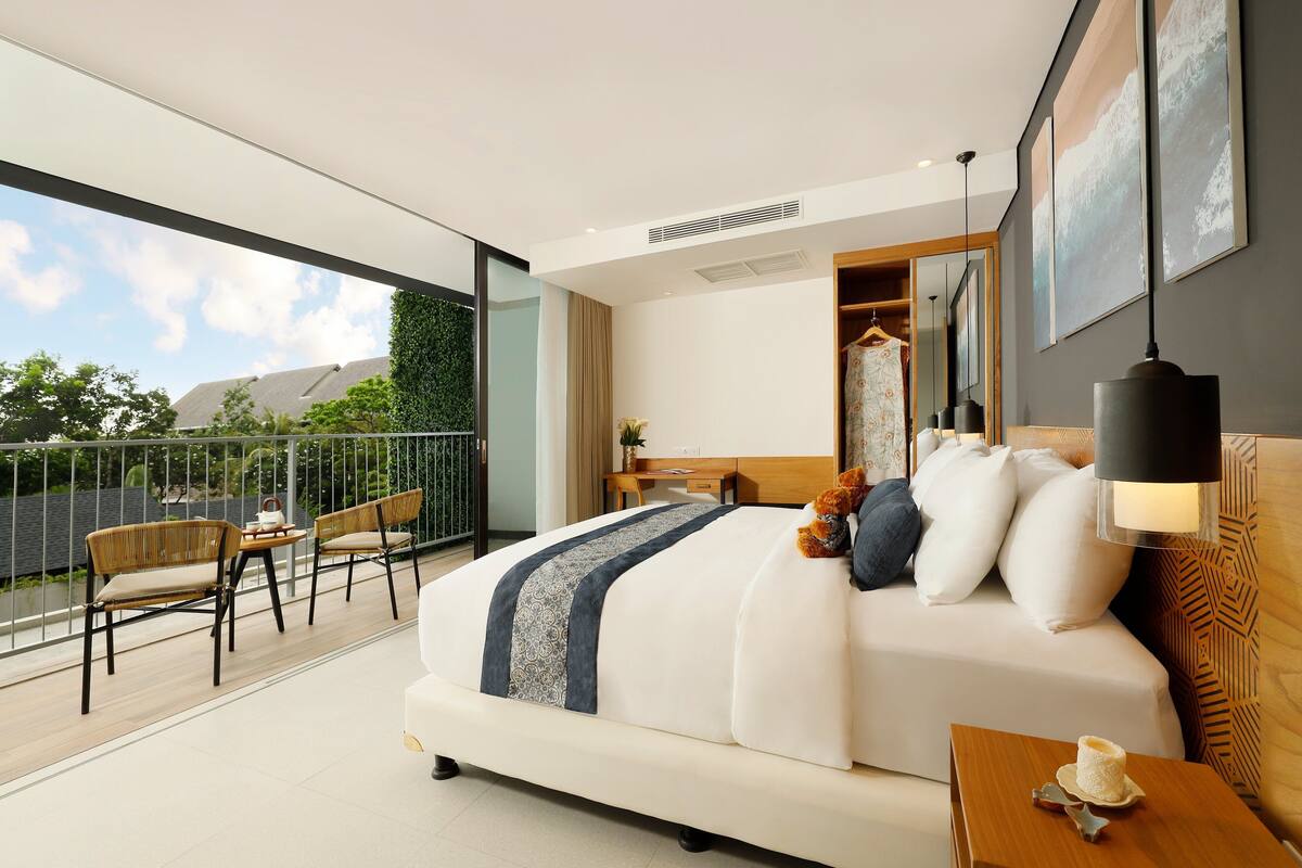 Una habitación de hotel moderna con una cama grande, un balcón con sillas y vista al cielo.