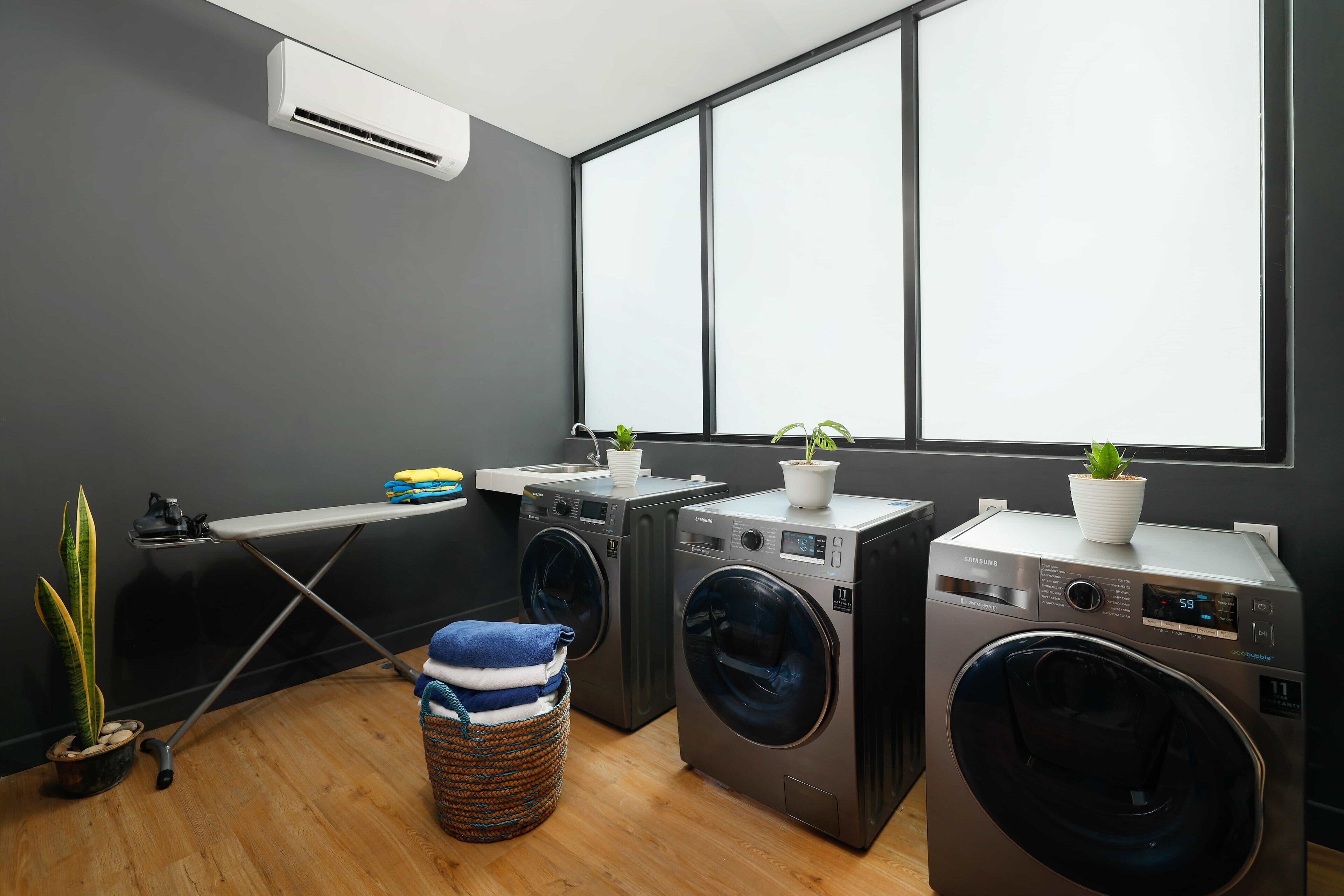 A laundry area with two front-loading washing machines, a drying rack, and a small ironing station.