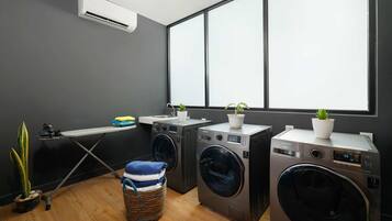 A laundry area with two front-loading washing machines, a drying rack, and a small ironing station.