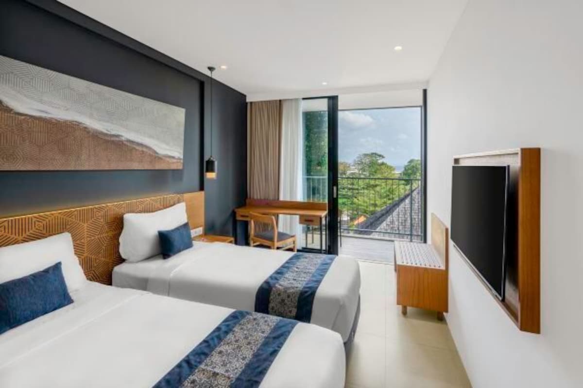 Ein modernes Hotelzimmer mit zwei Betten, einem Schreibtisch, einem Fernseher und einem Balkon mit Blick.