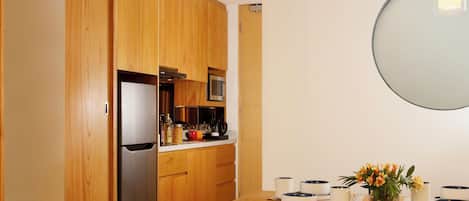 A modern kitchen with wooden cabinets, a stainless steel refrigerator, and a dining table set with plates and a vase of flowers.