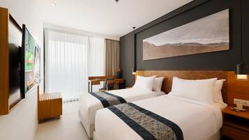 Habitación de hotel con dos camas, un escritorio, una silla, un televisor y un ventanal con cortinas.