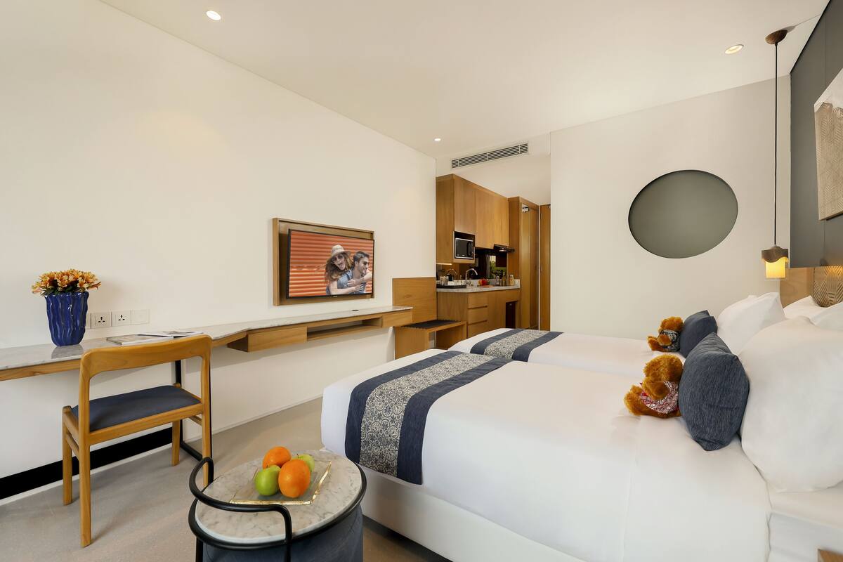 Una habitación de hotel moderna con cama, escritorio, silla, una pequeña mesa con fruta y un cuadro en la pared.