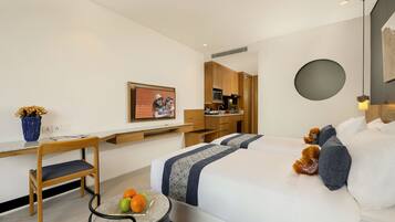 Una camera d'albergo moderna con un letto, una scrivania, una sedia, un tavolino con della frutta e un quadro appeso al muro.
