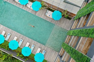 Vista aérea de uma piscina com espreguiçadeiras e guarda-sóis, cercada por vegetação e um deck de madeira.