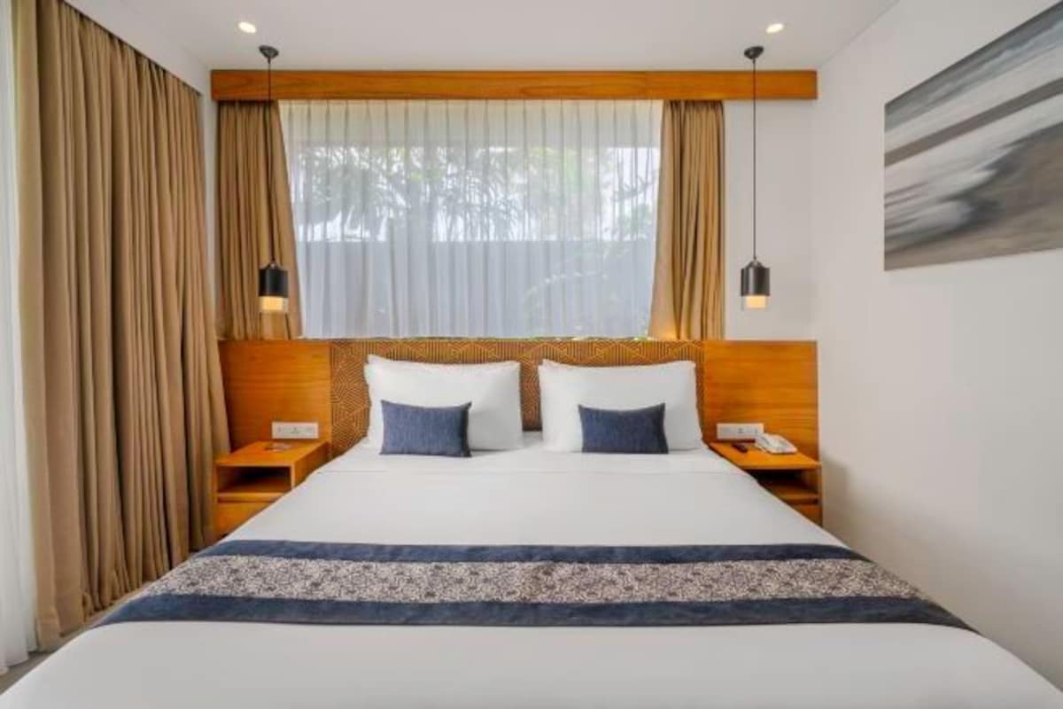 Ein Hotelzimmer mit einem großen Bett, einem Holzkopfstück, zwei Nachttischen und einem Fenster mit Vorhängen.