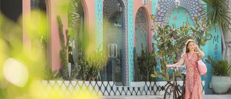 Una persona de pie junto a una bicicleta frente a un edificio con ventanas de arco y detalles decorativos.