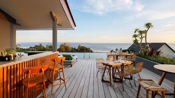 A wooden deck with a bar area, outdoor seating, and a view of the ocean. - Citadines Berawa Beach Bali Resort (Canggu)