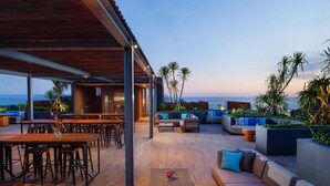 A rooftop lounge with wooden tables and chairs, a sofa area, and a view of the ocean. - Citadines Berawa Beach Bali Resort (Canggu)