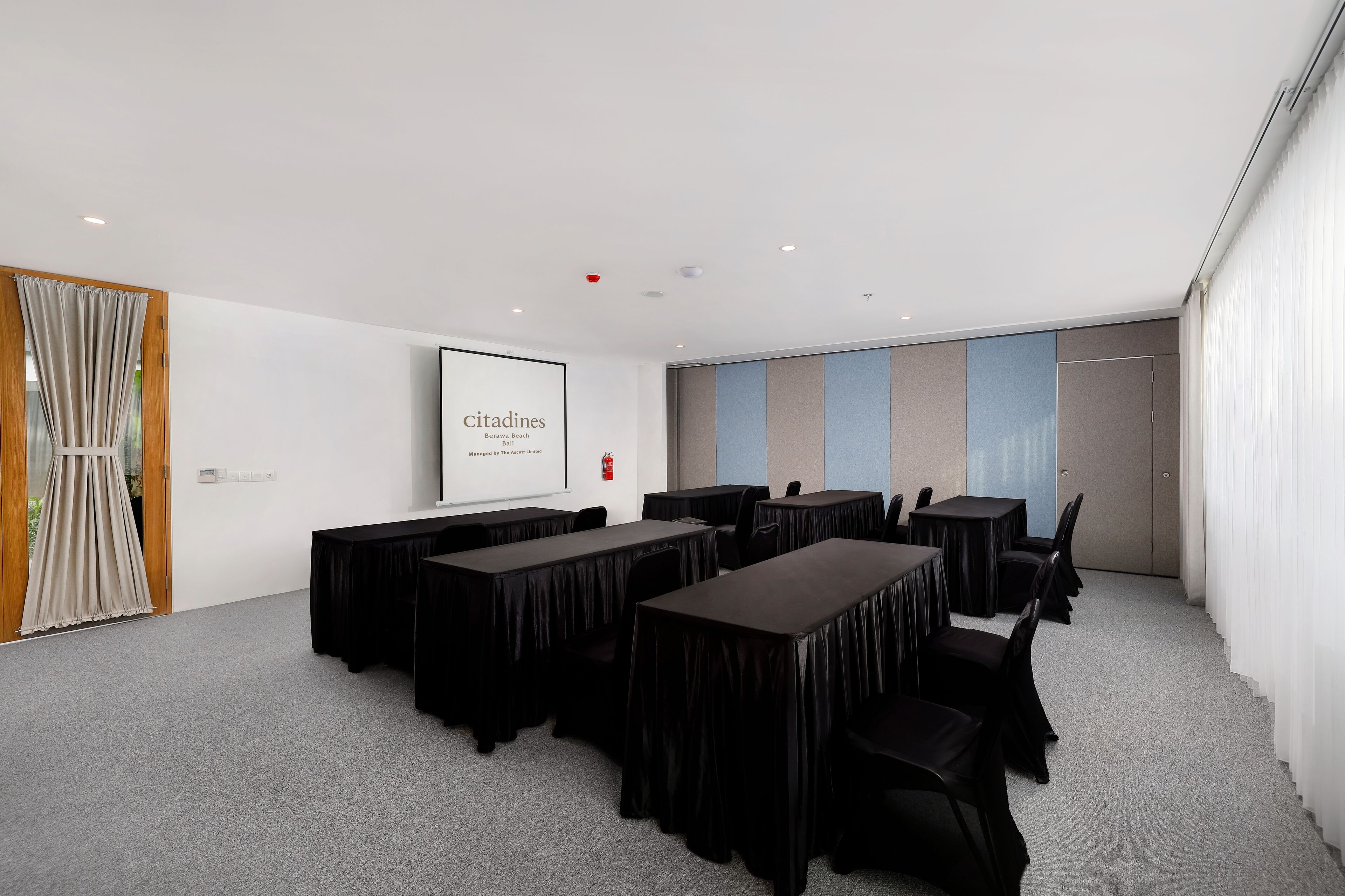 Un salón de conferencias con varias mesas y sillas, una pantalla de proyector y una pizarra.
