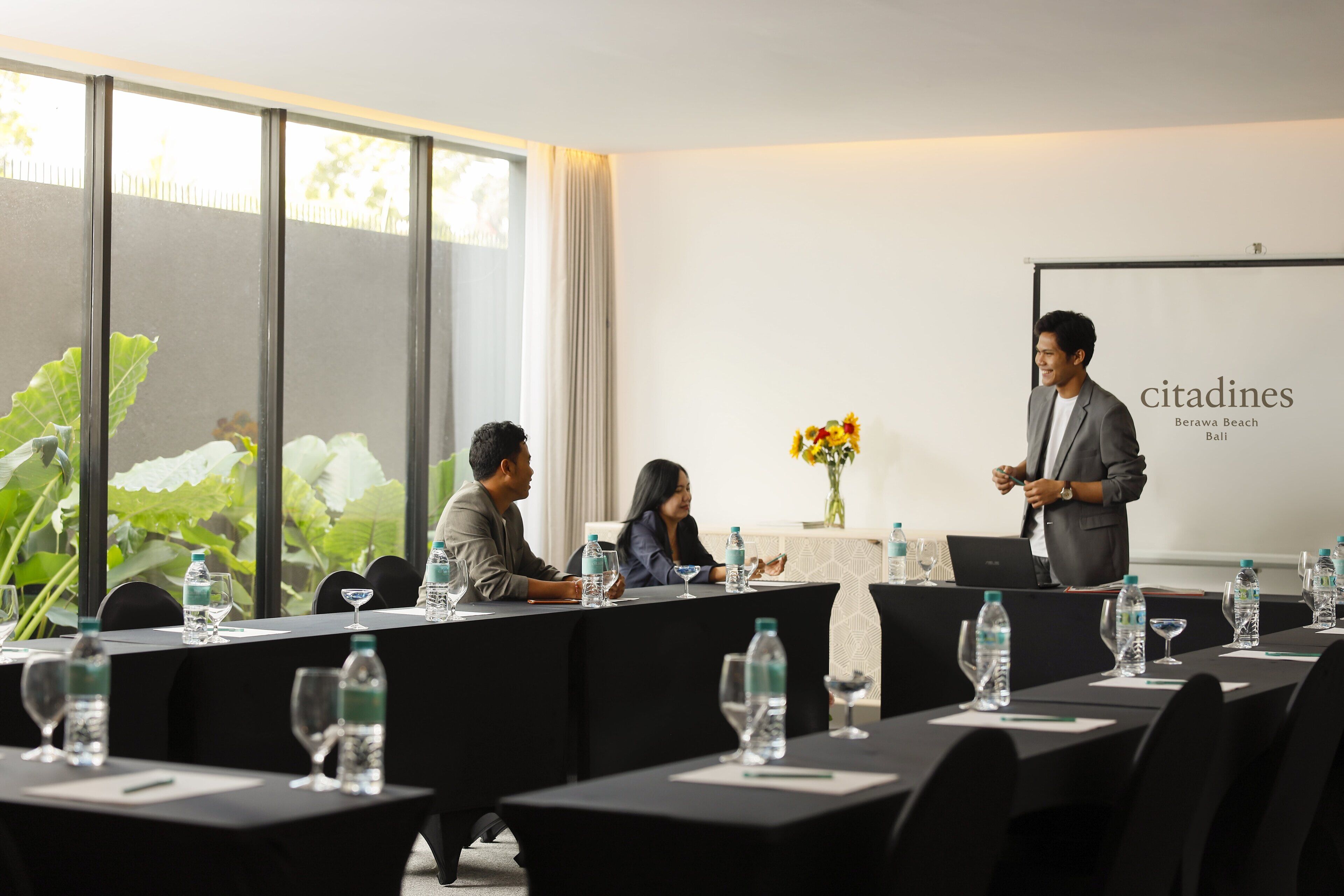 A conference room with a long table, chairs, water bottles, and a presentation screen.