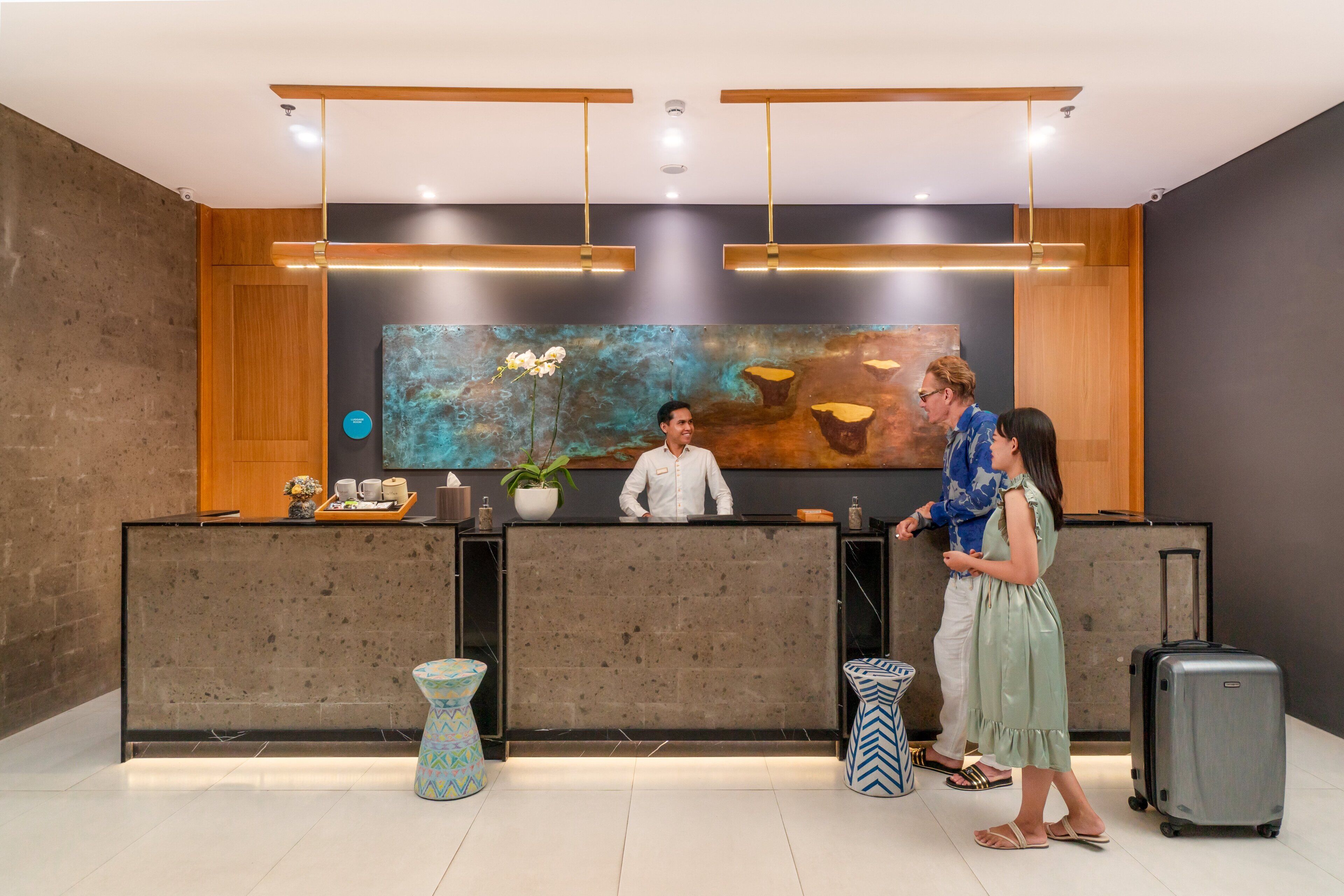 A reception desk with a modern design, a large abstract painting on the wall, and a potted plant.