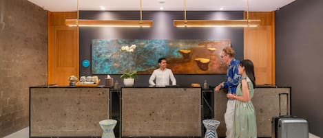 A reception desk with a modern design, a large abstract painting on the wall, and a potted plant.