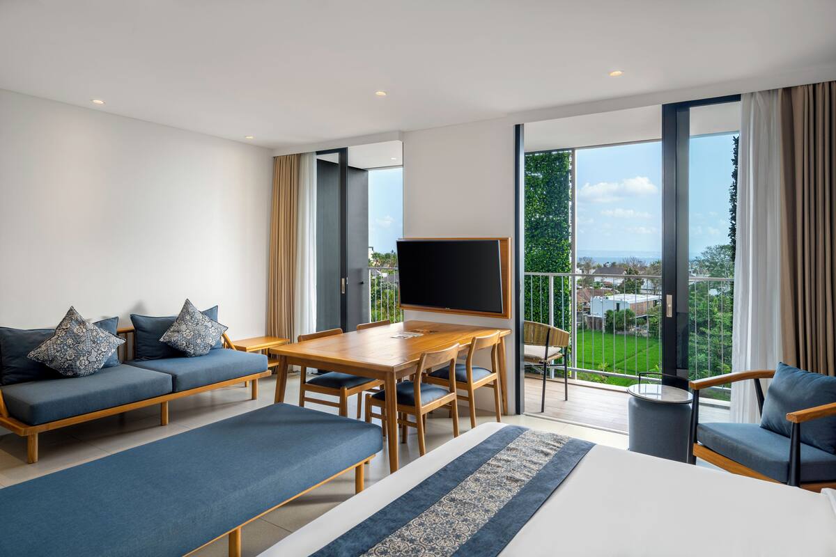 Un hotel moderno con una cama grande, un sofá, una mesa de comedor y un televisor. La habitación tiene ventanas amplias que ofrecen vistas al exterior.