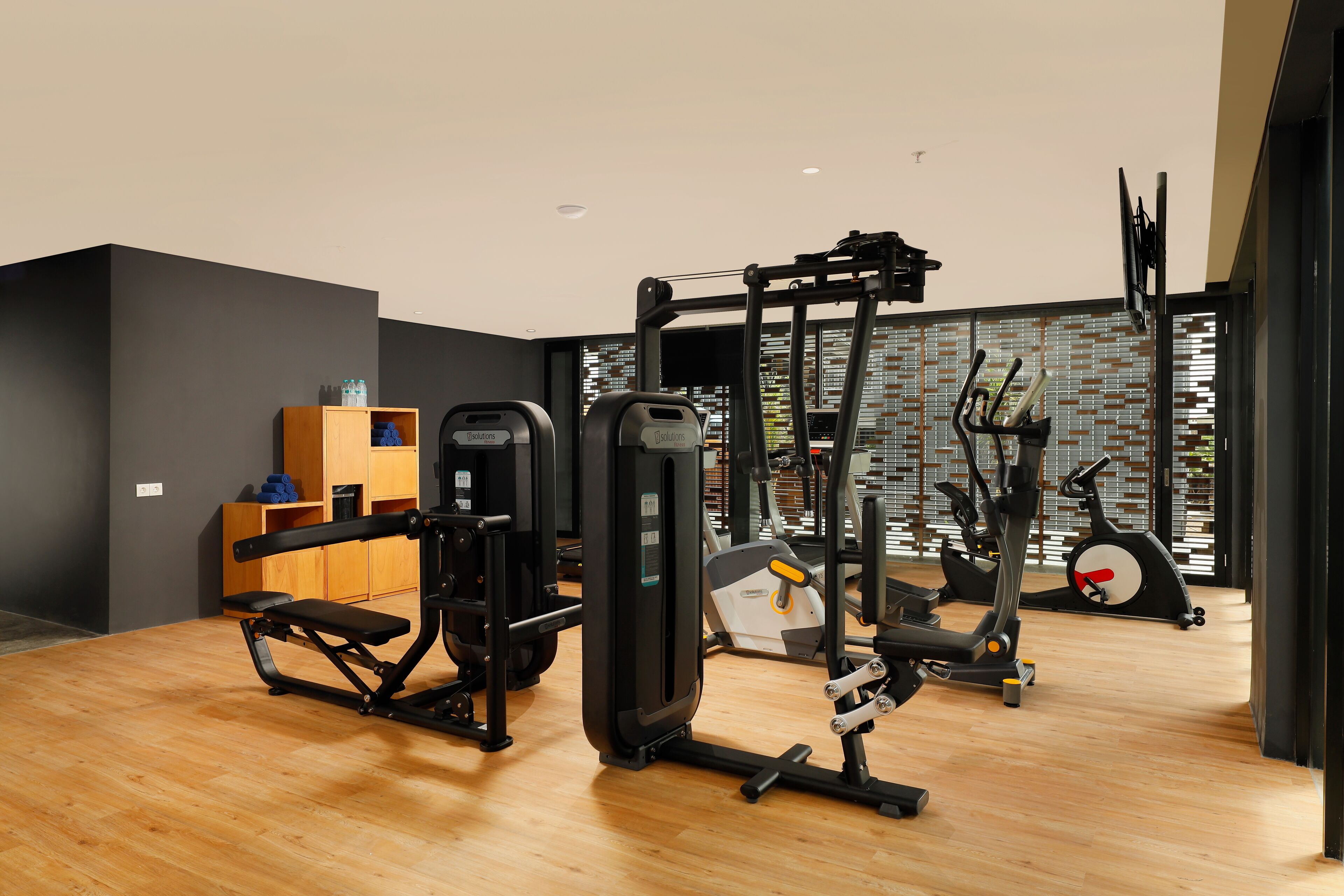 A modern gym with various exercise equipment, a wooden bench, and a brick-patterned wall.