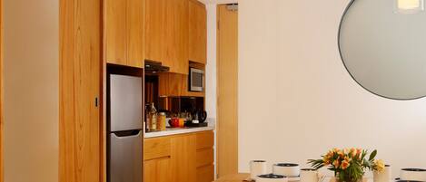 Una cocina moderna con armarios de madera, un refrigerador de acero inoxidable y una zona de comedor con una mesa lista para dos comensales.