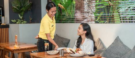 L’intérieur d’un restaurant avec des tables en bois, une personne servant des plats et un mur végétal.