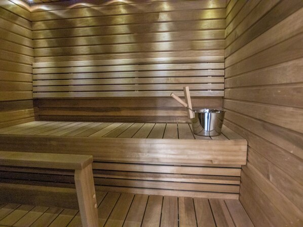 A sauna room with wooden benches and a metal bucket.