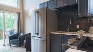 A modern kitchen with a stainless steel refrigerator, dark cabinetry, and a large window. - 2 BDR w Loft / Incredible Views / Family-Friendly (Fernie)