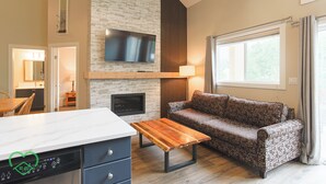 A modern living room with a fireplace, sofa, and a TV mounted on the wall. - 2 BDR w Loft / Incredible Views / Family-Friendly (Fernie)