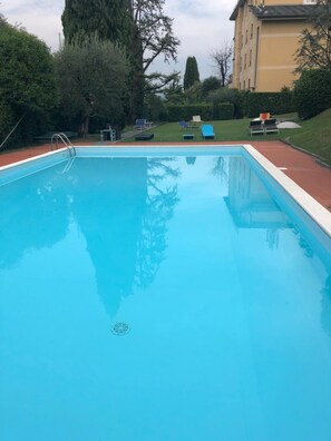 Una piscina rettangolare con una scala in metallo su un lato, circondata da un solarium rosso. Si vedono diversi lettini e un tavolino sullo sfondo.