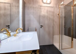 Un bagno con un lavandino bianco, rubinetteria dorata e box doccia in vetro.