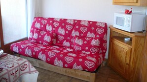 Ein gemütliches Zimmer mit einem rot gemusterten Sofa, einer Mikrowelle auf einem Holzkabinett und einem Tisch mit einer gemusterten Tischdecke.