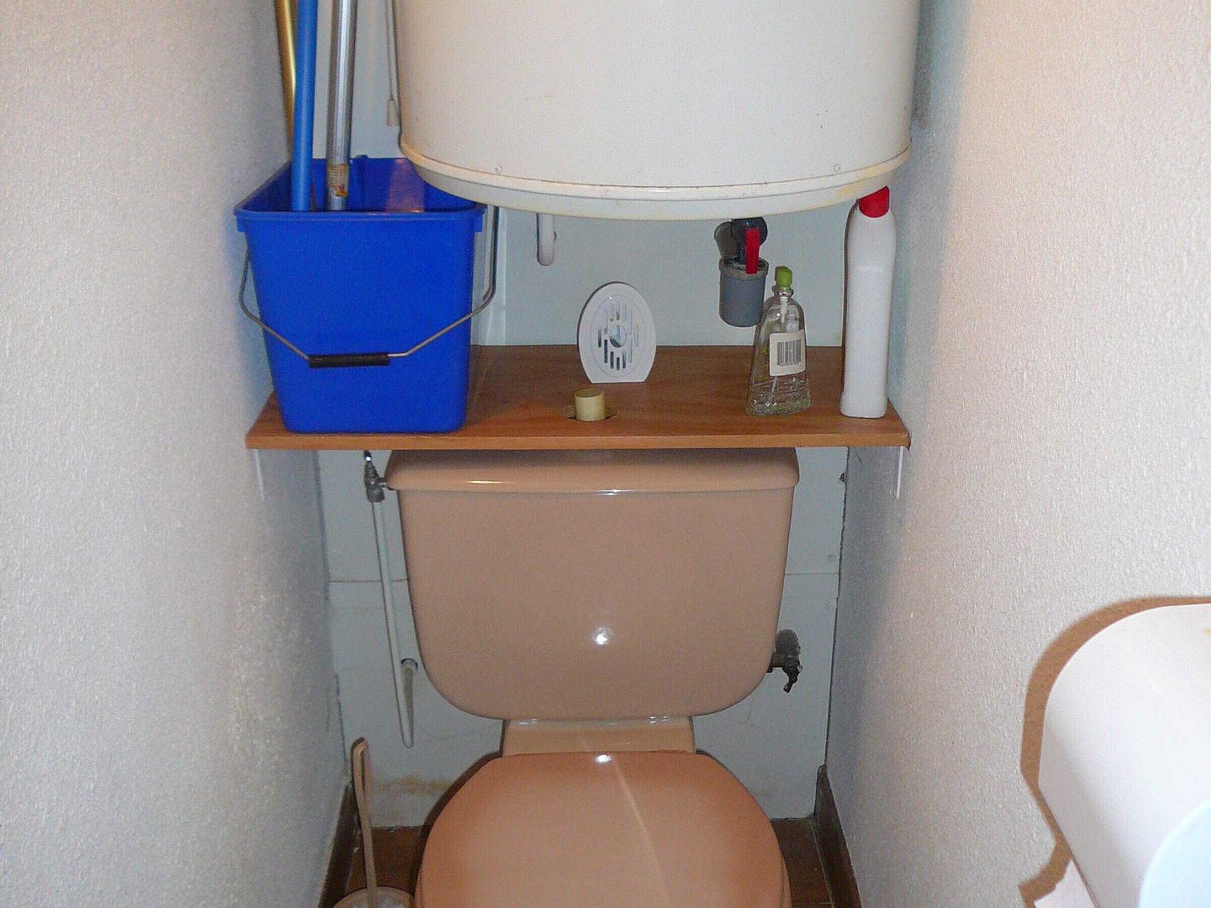 A small bathroom with a toilet, a blue bucket, a white sink, and a mirror.