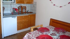 Eine Küche mit Holzausstattung, einer Mikrowelle und einem Spülbecken. Ein Esstisch ist mit Geschirr in Rot gedeckt.