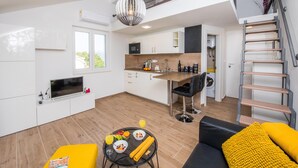 Et moderne køkken med spiseplads, en trappe og en stue med sofa samt et bord dækket med mad og drikkevarer.