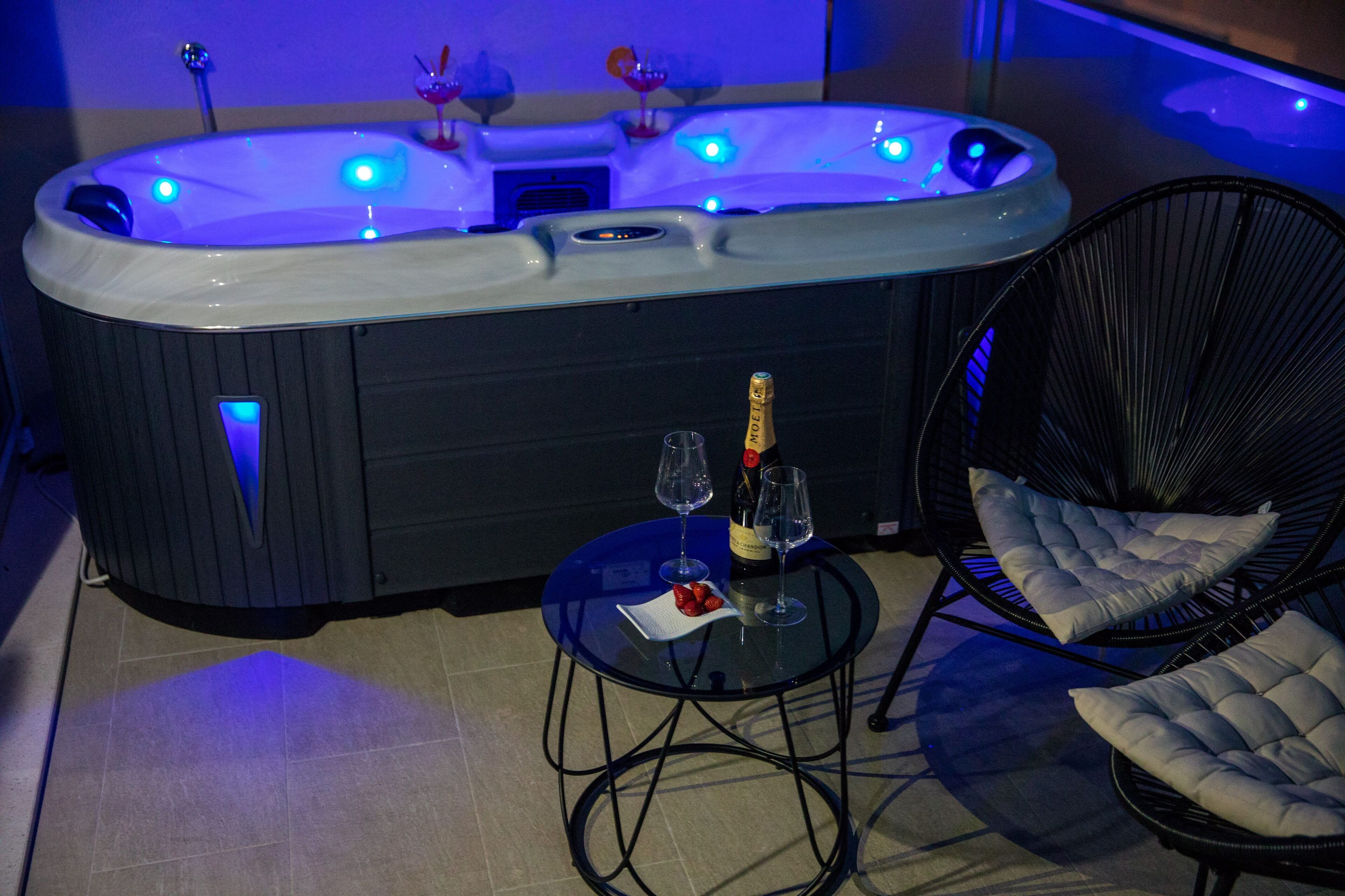 Ein Whirlpool mit blauer Beleuchtung, eine Champagnerflasche, zwei Weingläser und eine kleine Schale mit Erdbeeren.