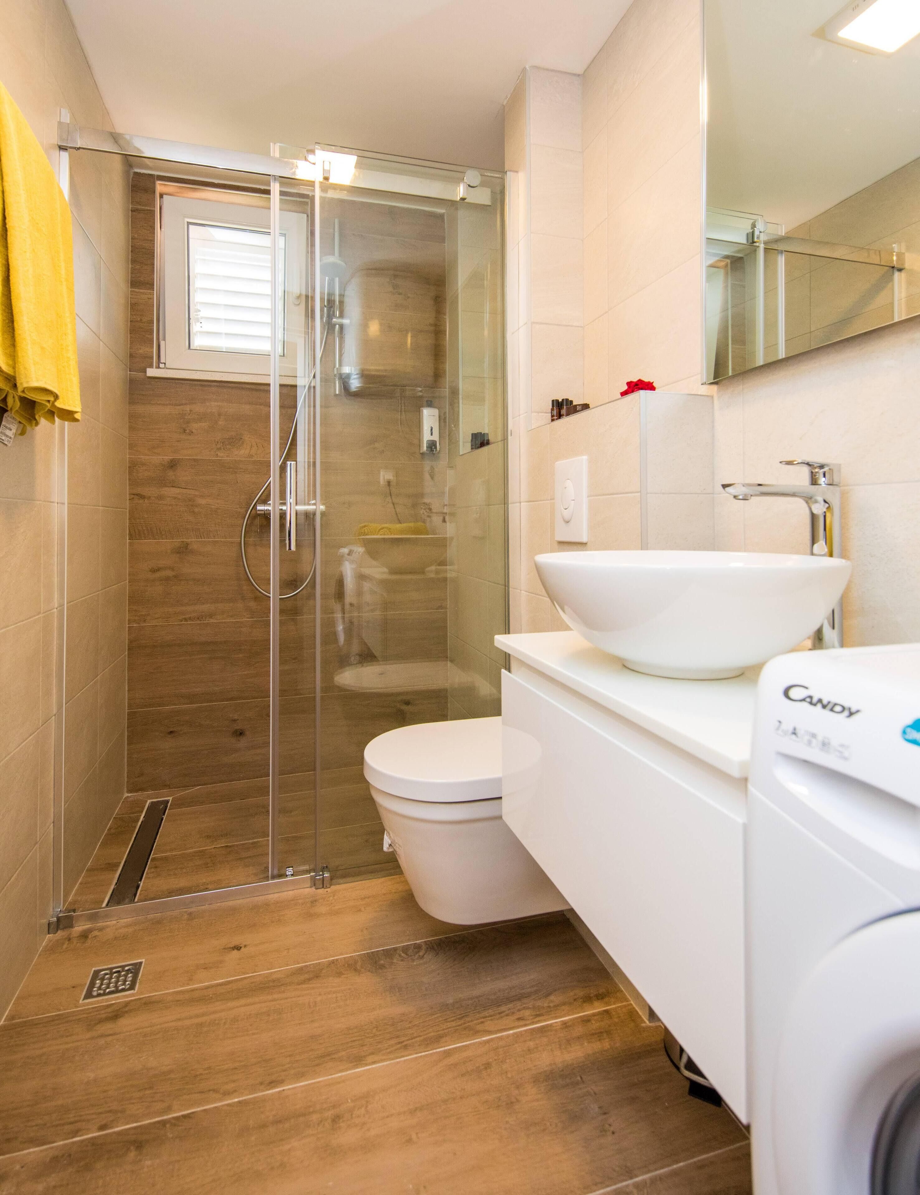 Een moderne badkamer met een glazen douchecabine, een wit wastafelmeubel en een toilet.