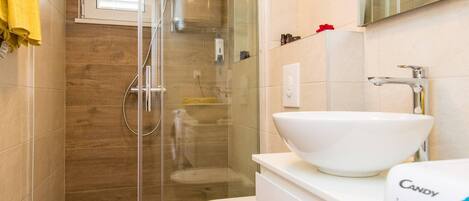 Een moderne badkamer met een glazen douchecabine, een wit wastafelmeubel en een toilet.