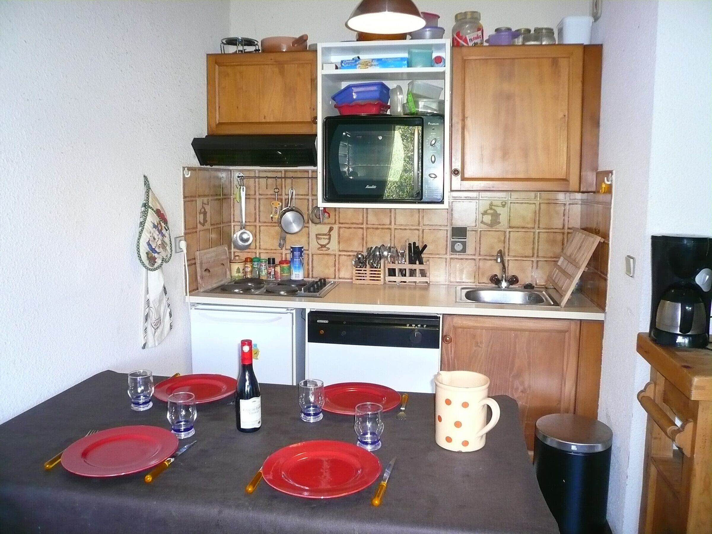 Eine kompakte Küche mit Herd, Mikrowelle und Spüle. Oberhalb der Arbeitsplatte befinden sich Schränke und darunter ein kleiner Kühlschrank.