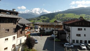 A view of a town with traditional buildings, a parking area, and a mountain range in the background.