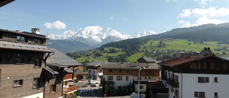 A view of a town with traditional buildings, a parking area, and a mountain range in the background.
