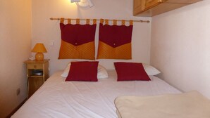 A bedroom with a bed, two pillows, a nightstand with a lamp, and a wooden cabinet above the bed.