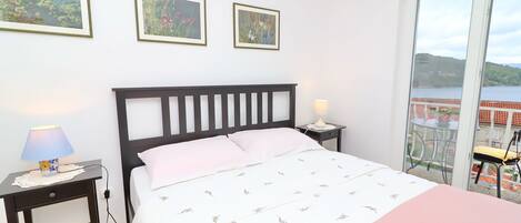 A bedroom with a bed, a nightstand with a lamp, and a view of a balcony with a table and chair.