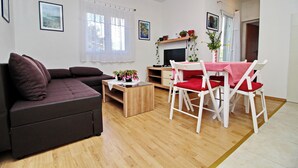 Ein modernes Wohnzimmer mit einem dunkelbraunen Sofa, einem Holztisch und einem Essbereich mit weißen Stühlen und einer roten Tischdecke.